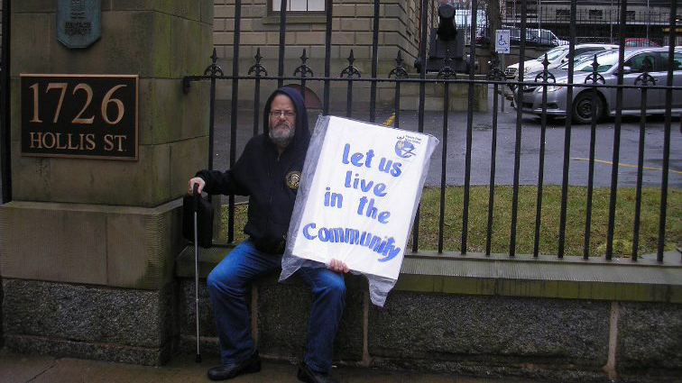 A man is sitting on a bench holding a protest sign.