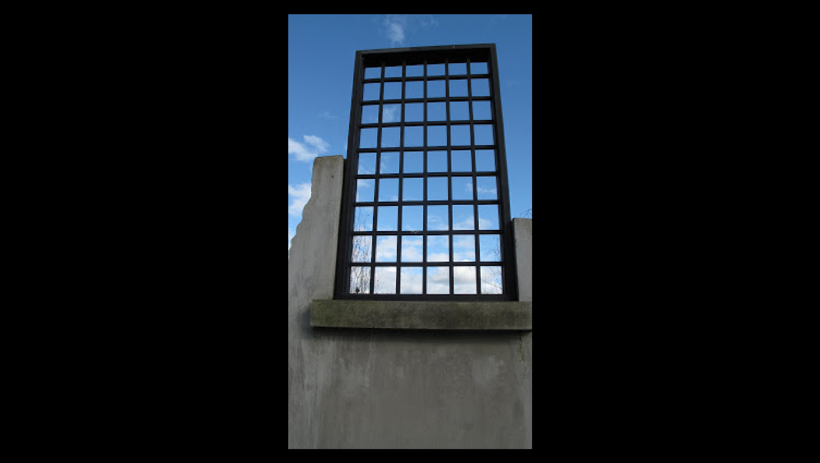 A large window with bars stands on top of a concrete wall.