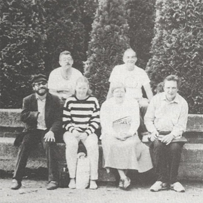 Six people posing for a photo on a park bench