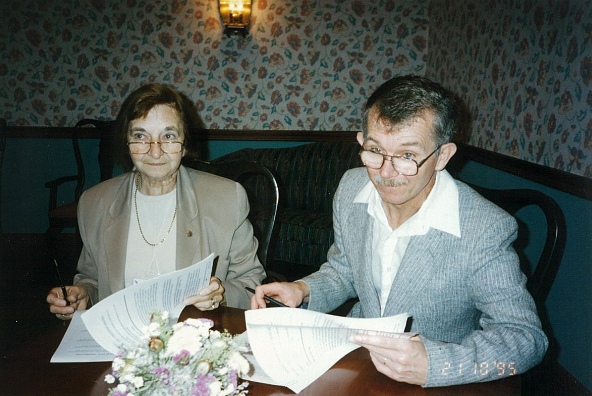 A man and woman sit at a table signing documents.